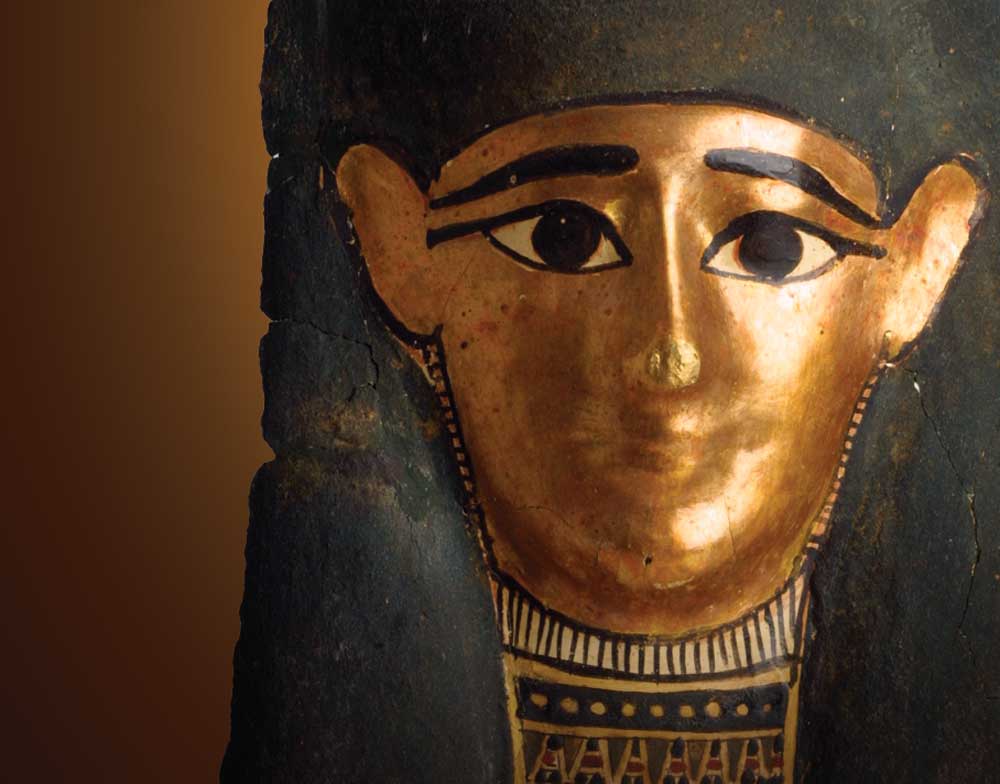 Detail image of a Gilded Mummy Mask from the Senusret Collection on the right side of the image with a brown and gold background