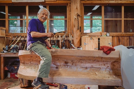Photo of artist Nathan Jackson sitting on a piece of wood carving in a woodshop