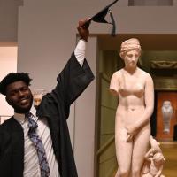 Student Lonnie Reid is shown holding his graduation cap in his left hand over one of the sculptures in our Greek and Roman art Gallery