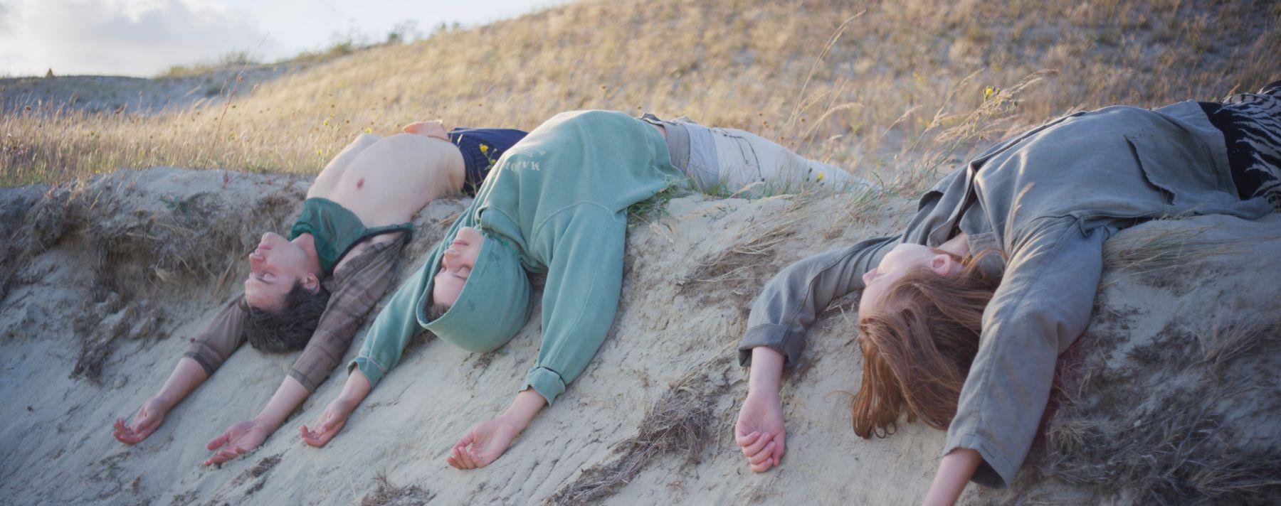 Still image from Songs from the compost with three figures laying on their backs with their arms extended above their head  