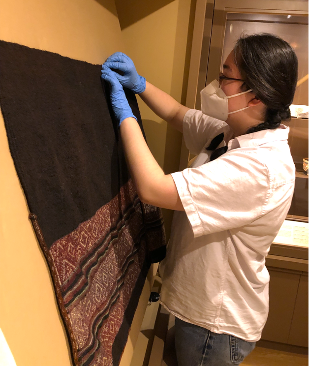 Claudia Konig installs a textile in the Art of the Americas galleries 