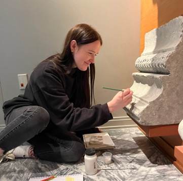 Intern Elise sits on the floor cleaning and repairing a painted plaster cast in the museum 
