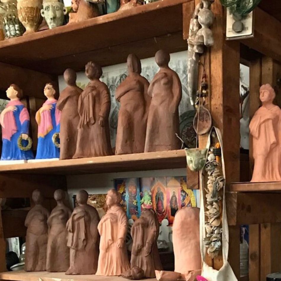 Image of clay sculptures inspired by Tanagras in various stages of completion shown on shelves in a studio 