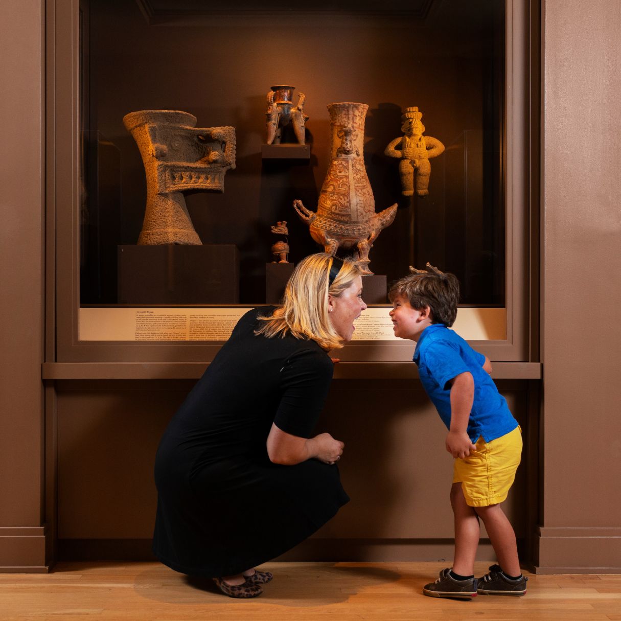 Adult and child looking at each other and smiling in the galleries in front of sculptures