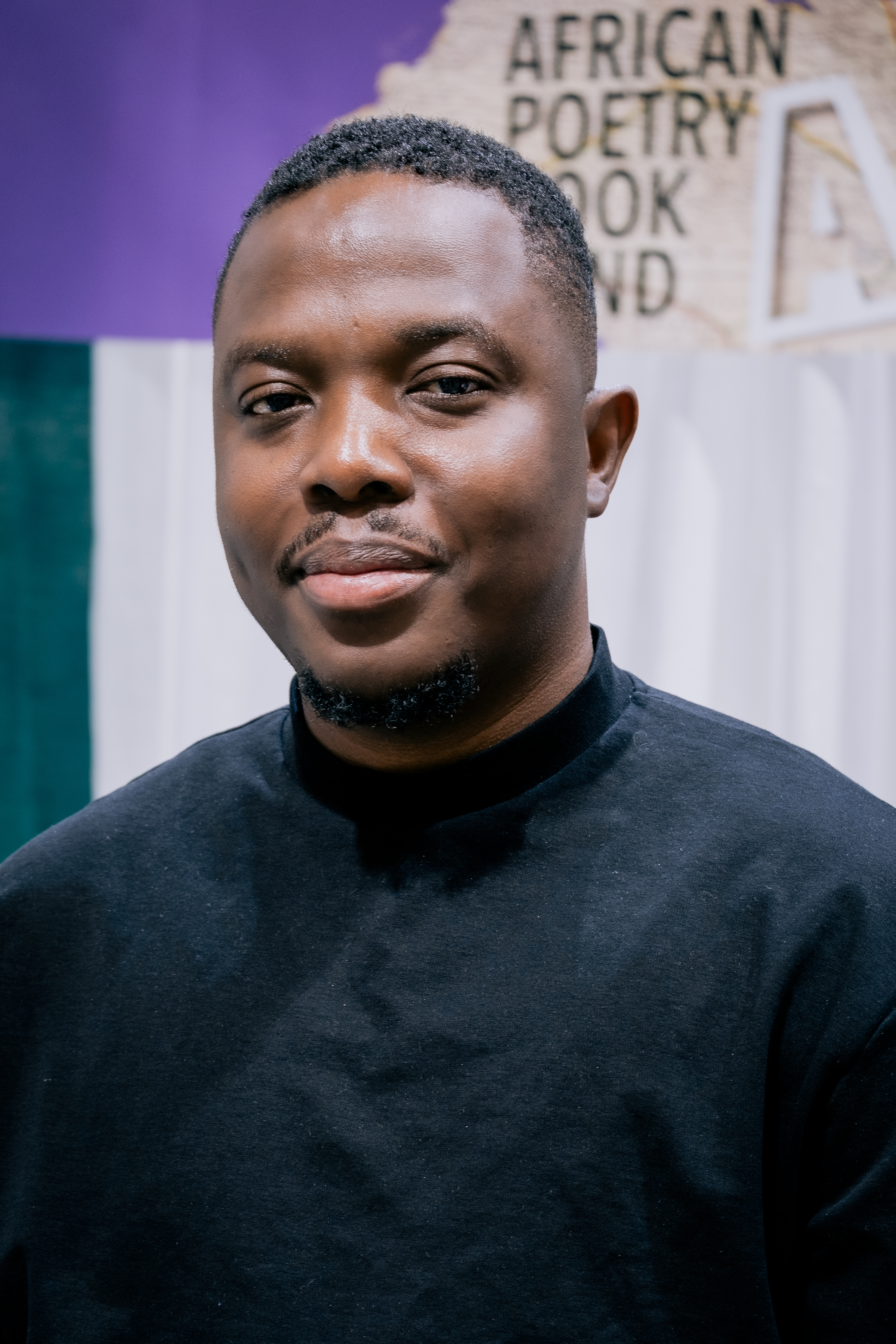 Photo of Romeo Oriogun wearing a black shirt with a collaged work in background