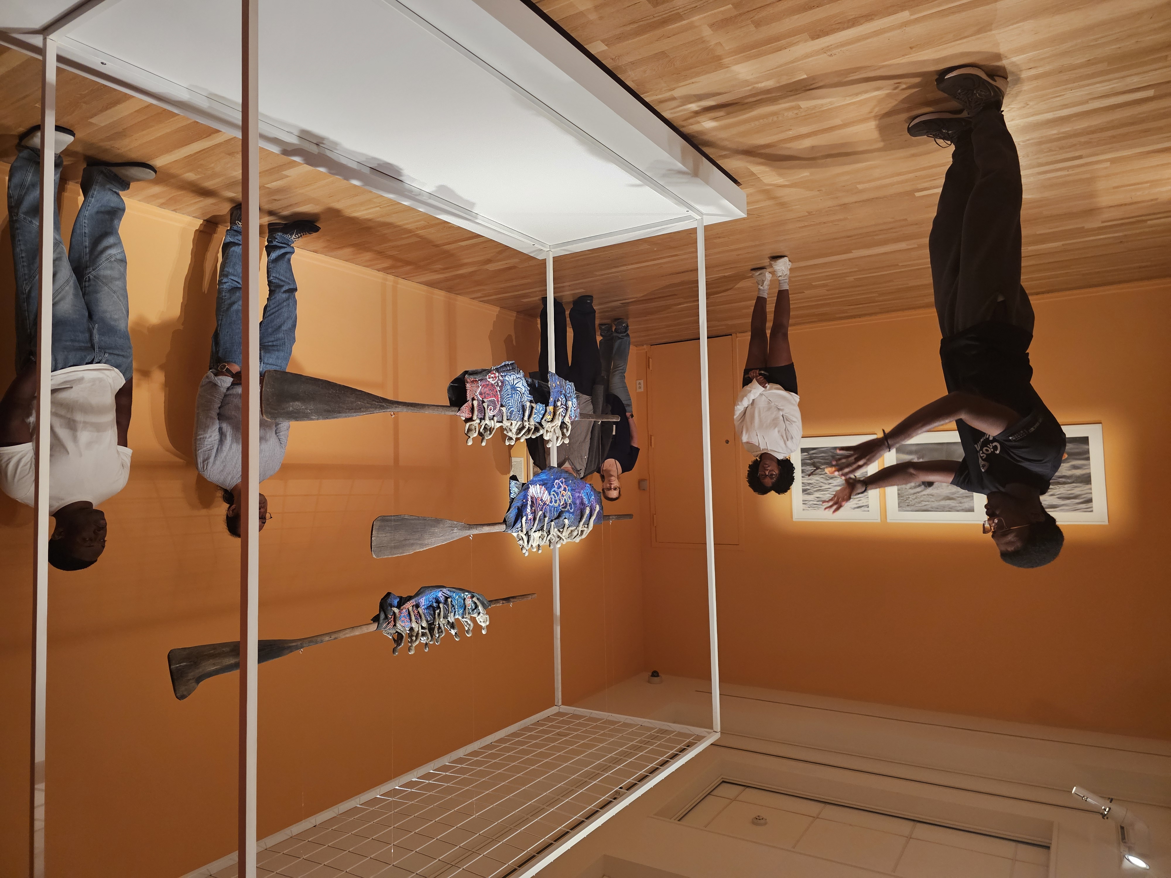 Image of a student guide leading a tour pointing at a sculptural work in a gallery with orange walls