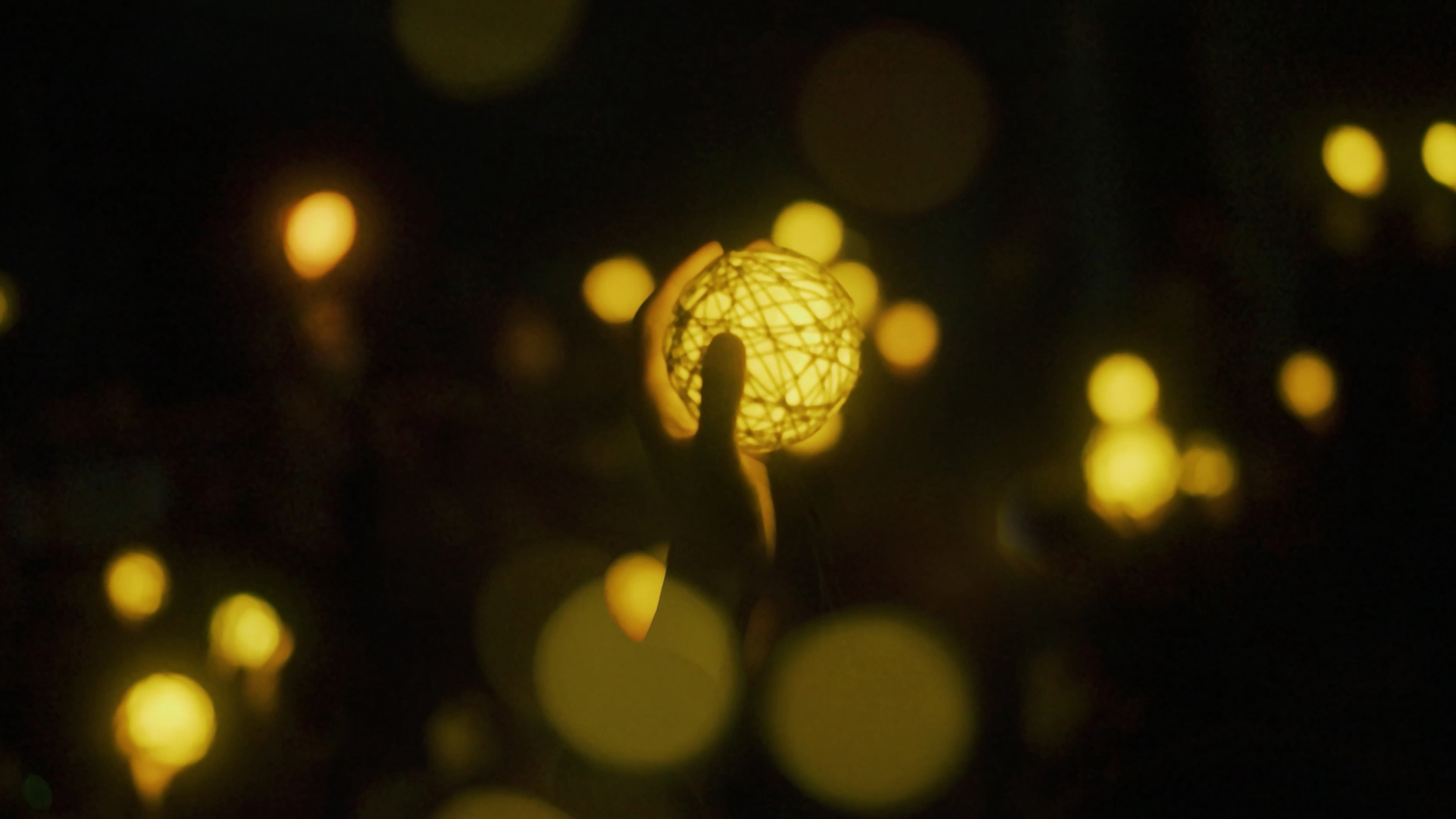 Installation of  INOCHI THEATER:If Life were Light by Aru Inc. with a dark background and circular spots of yellow light, a hand holding a yellow ball of light in the center