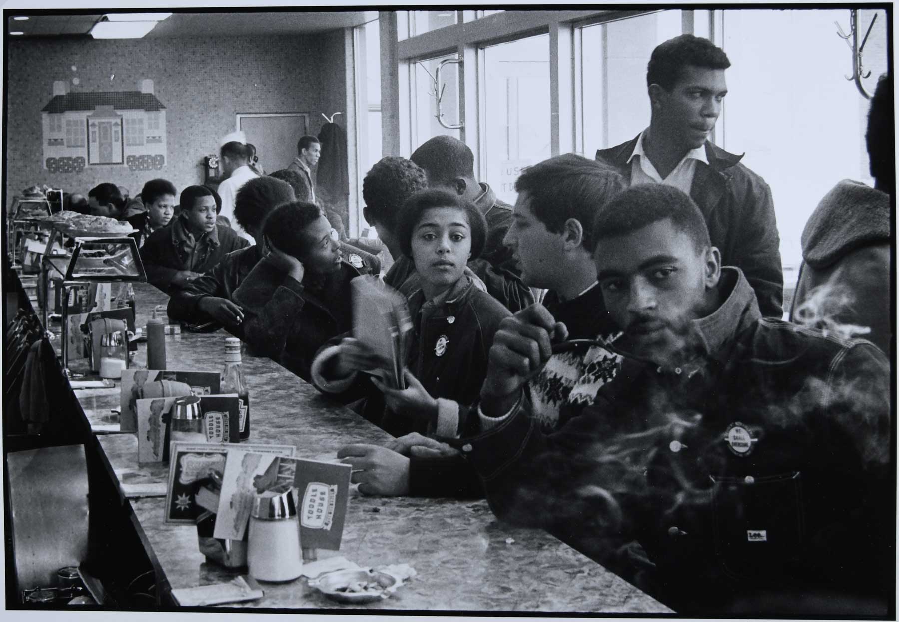 Black and white photo by Danny Lyon of a sit-in at a Toddle House in Atlanta, GA, 1963 showing a crowded counter full of people