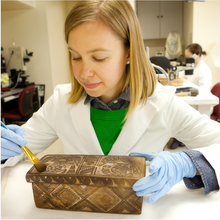 Ashley Jehle cleaning an object on a table in the conservation lab