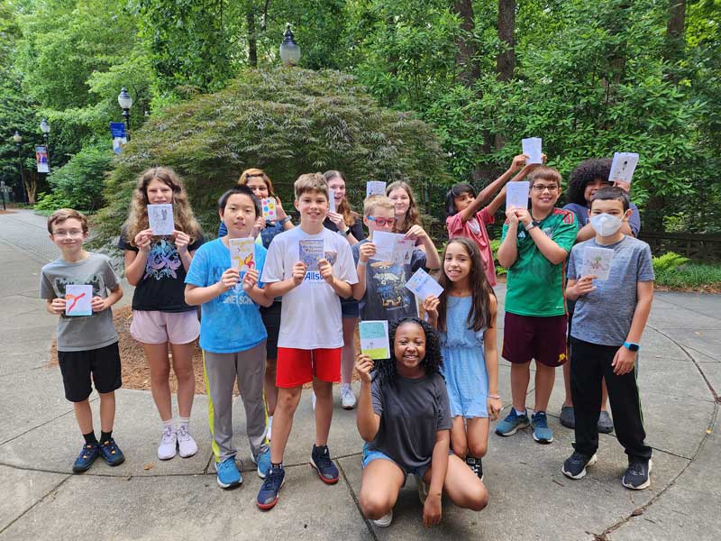 Camp Carlos participants are outside holding up their stories created during the sequential art camp in summer 2023