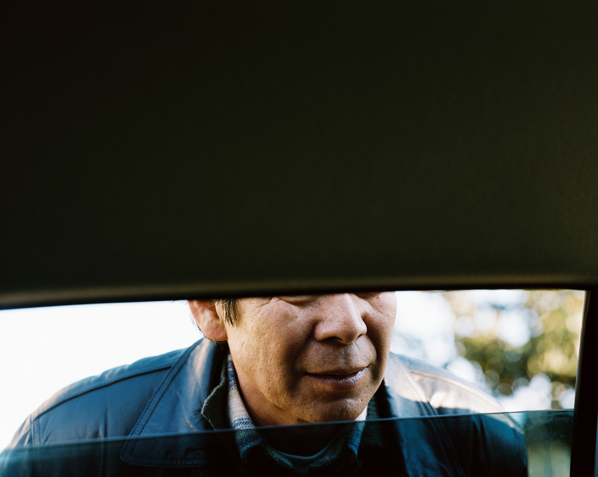Photo by Shingo Kanagawa from his father series showing his fathers face as through an open car window, his face obscured hiding his eyes