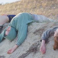 Still image from Songs from the compost with three figures laying on their backs with their arms extended above their head  