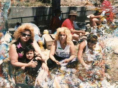 Color photograph. In the image there are four seated figures. On the left there is a mother holding her young daughter in her lap. In the center there is a blonde woman sitting crossed-legged, looking at the camera. The forth figure on the right is a man sitting, looking down. The color photo has some water damage and discoloration across the surface of the photograph.