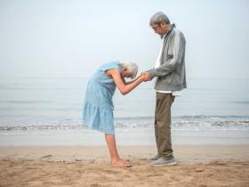 Photo of woman and man standing on a beach facing eachother, the women in bowing her head and the couple is clasping one another's hands r© Manjari Sharma, 2020.
