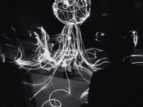Black and white image of people interacting with a light piece by Kosuke Matsushima
