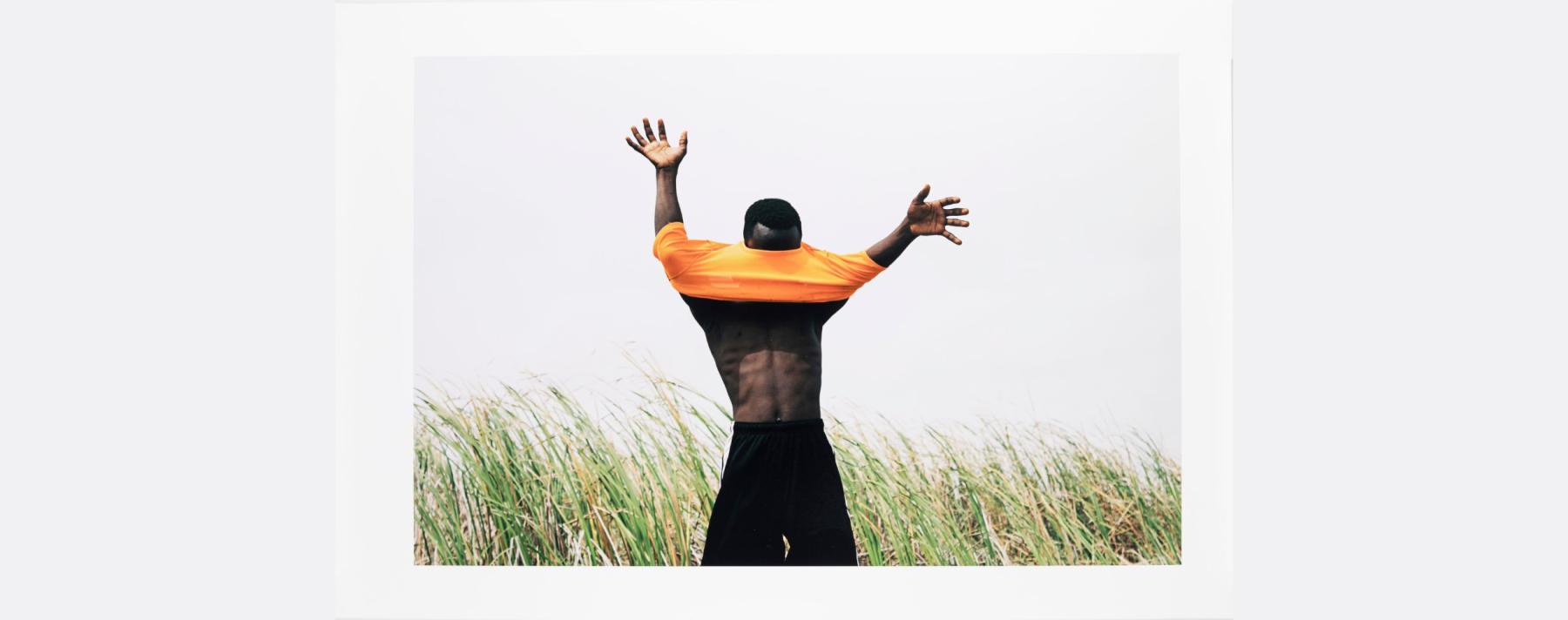 Nana Yaw Oduro  Inkjet print titled PHILIP showing person with arms outreached, an orange shirt covers the face, tall grass is swaying in the background