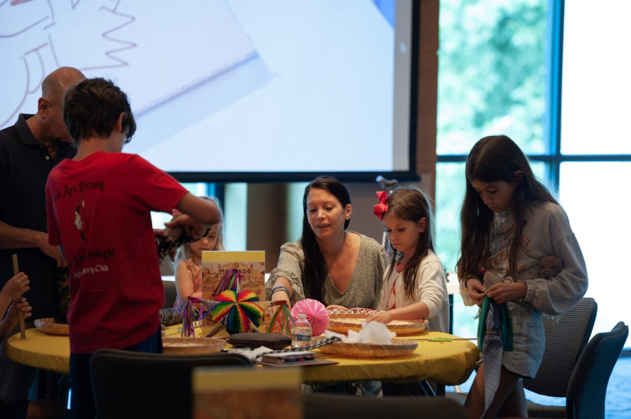 a group sits around a table creating things with colored materials 
