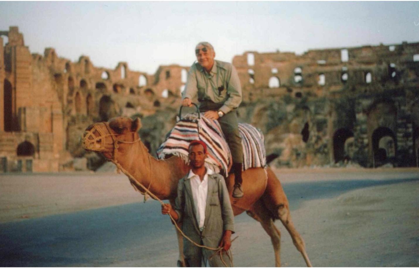 Photo of Dr. John Ridley riding a camel in front of the amphitheater in Tunisia circa 1972